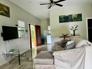 A living room with a flat-screen TV, a glass coffee table, a sofa with cushions, and artwork on the walls. - Charming 3-bedroom Villa-5 beds-AC - 7minutes drive to San Ignacio- Restaurant (Belize)