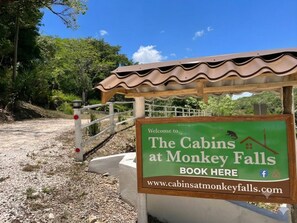 A welcome sign for The Cabins at Monkey Falls with a website URL and a Facebook icon.