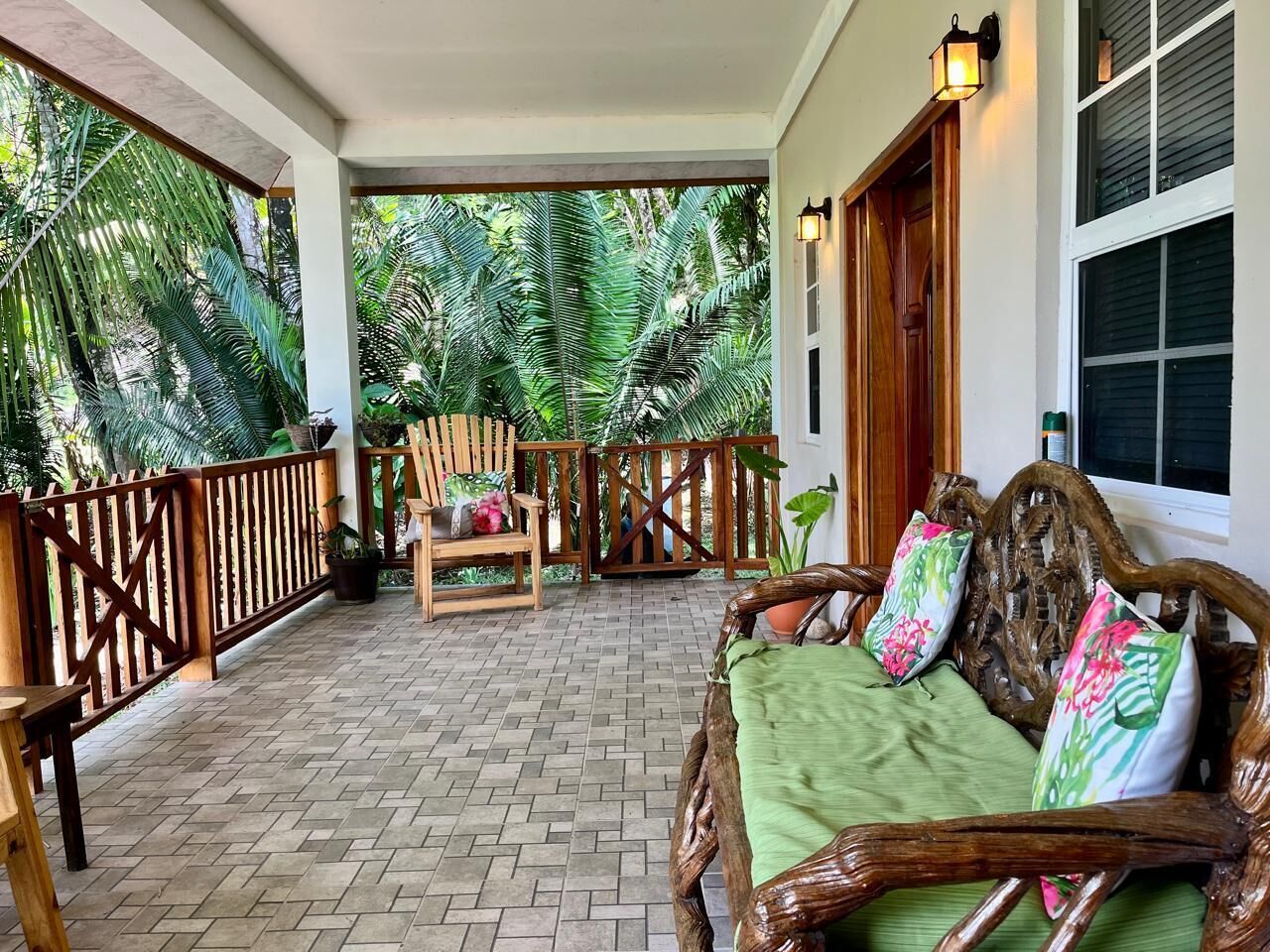 A covered porch with a wooden bench and a sofa, surrounded by a wooden railing and potted plants.