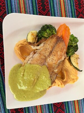 A plate of food with a piece of meat, vegetables, and a green sauce.