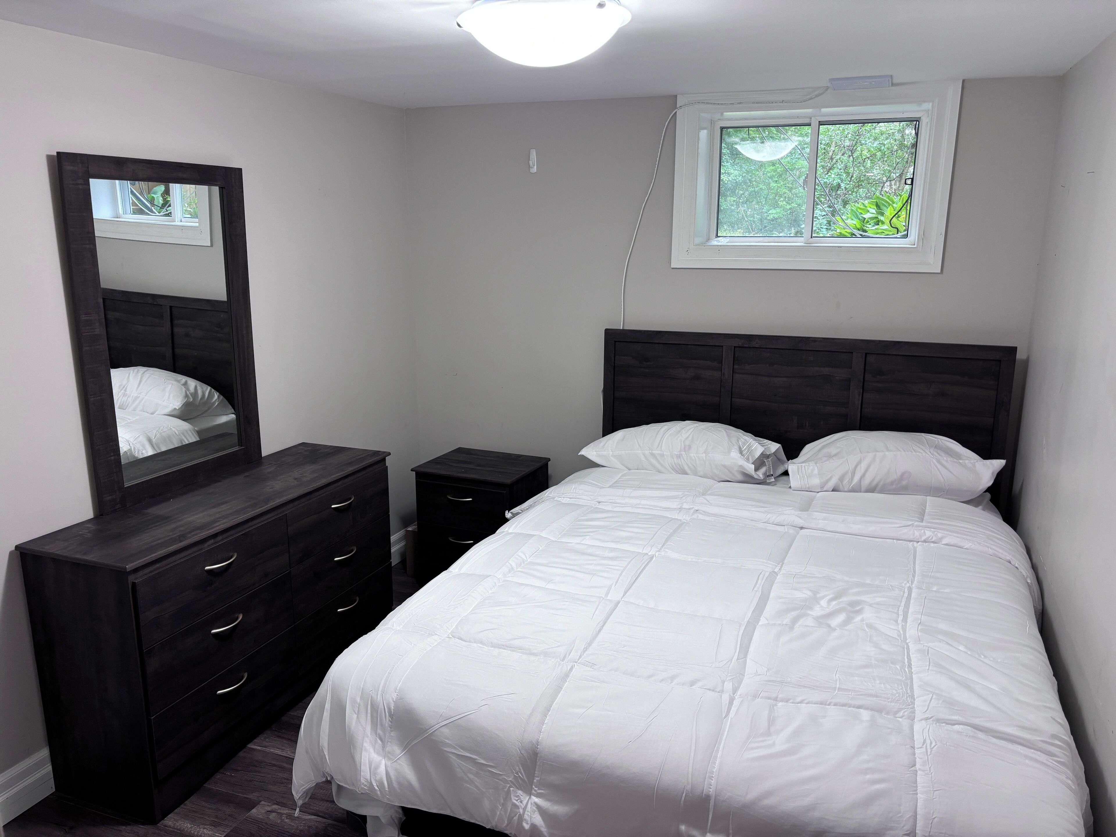 A bedroom with a bed, a dresser, a nightstand, a mirror, and a window.