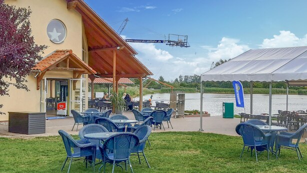 An outdoor seating area with tables and chairs, a covered patio, and a view of a lake. - Nice home in Neubrandenburg with WiFi (Neubrandenburg)