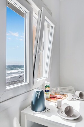 A room with a white table set for breakfast, a view of the beach, and a window with a white frame. - Home2Book Stunning BeachFront Apt, Pozo Izquierdo (Pozo Izquierdo)