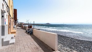 A coastal walkway with a pebble beach, a clear sky, and a distant mountain. - Home2Book Stunning BeachFront Apt, Pozo Izquierdo (Pozo Izquierdo)