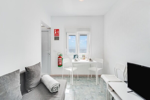 Ein kleiner, sauberer Raum mit einer Couch, einem Tisch mit Stühlen, einem Fernseher und einem Fenster mit Aussicht.