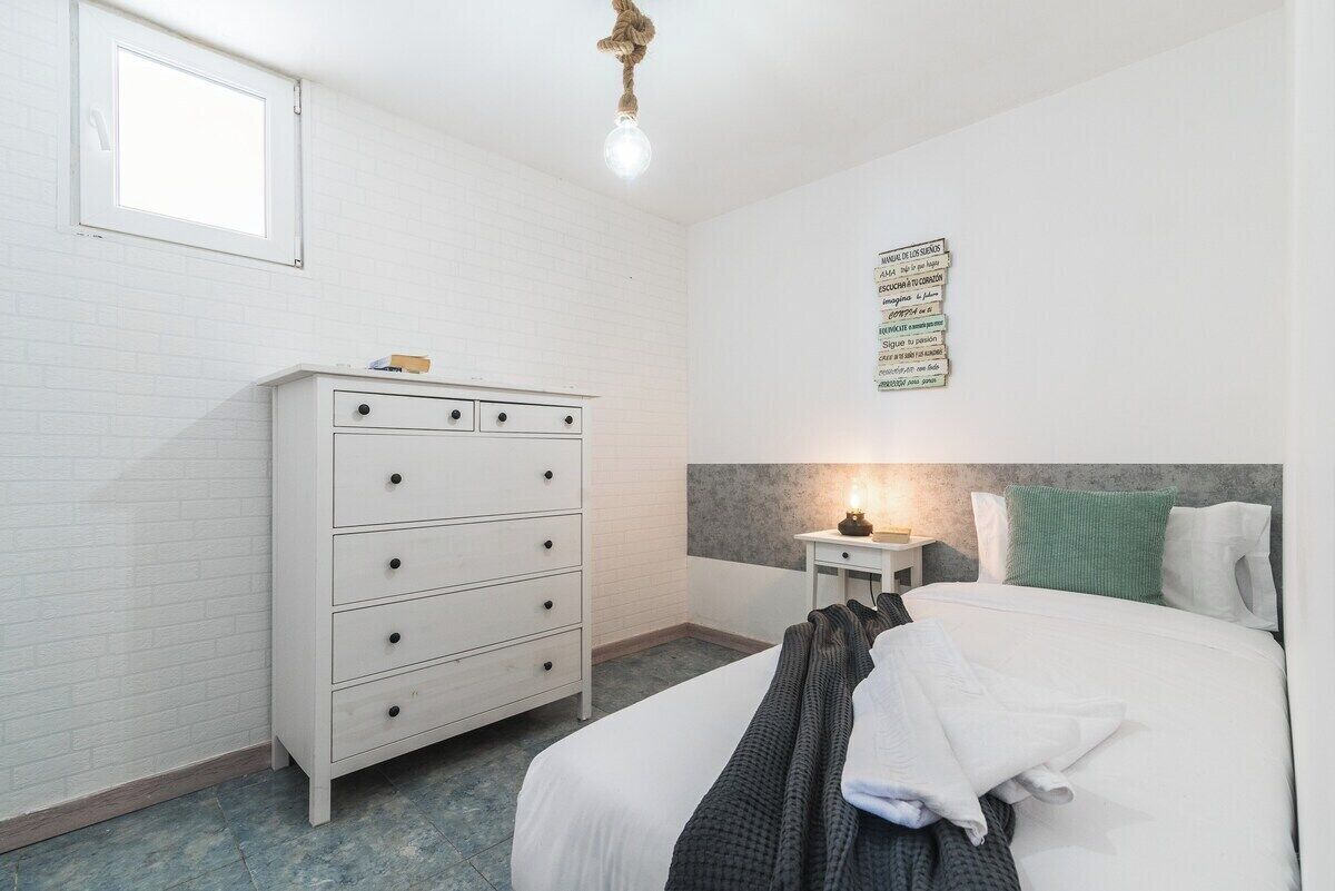 Ein Schlafzimmer mit Bett, Kommode, Nachttisch, Wanduhr und Fenster.