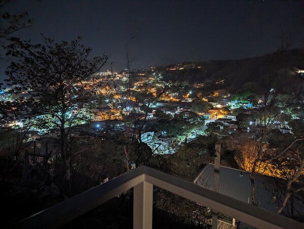 Vista noturna de uma cidade com edifícios iluminados e uma colina imponente ao fundo.