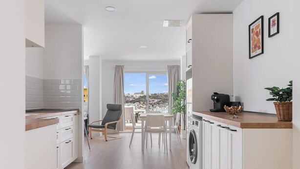 A modern kitchen with a dining area, large windows, and a view of the city.