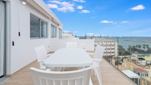 A balcony with a white table and chairs, overlooking a marina and buildings.
