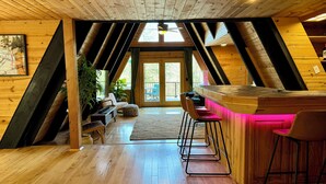 A cozy attic-style room with wooden floors, a bar area with stools, and a view of the outdoors through a large door. - A-Frame On The Rocks. Hot Tub. Payson. Waterwheel. (Payson)