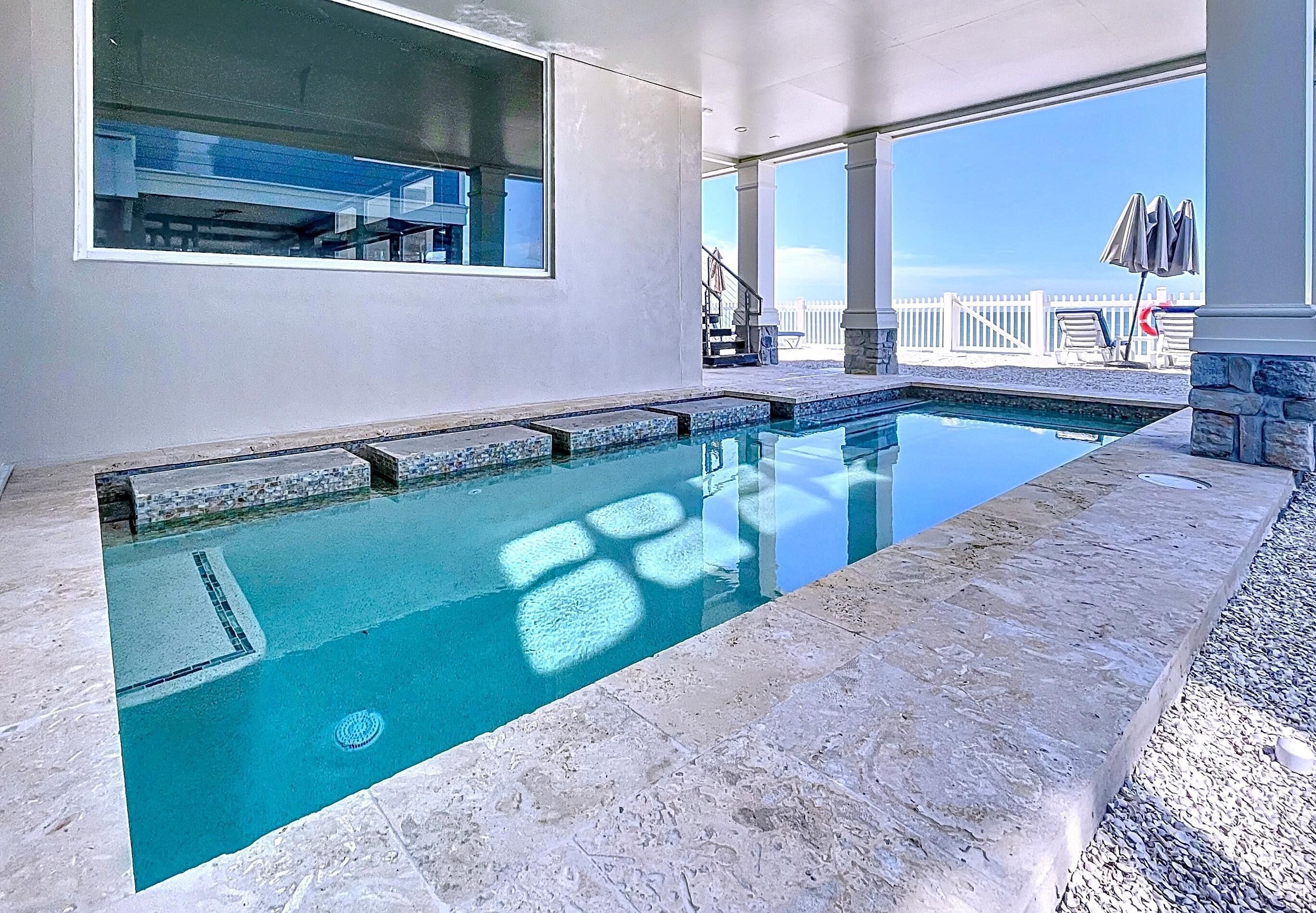 Une piscine rectangulaire à l’eau d’un bleu limpide, entourée de carreaux de pierre et bordée d’un mur en pierre.