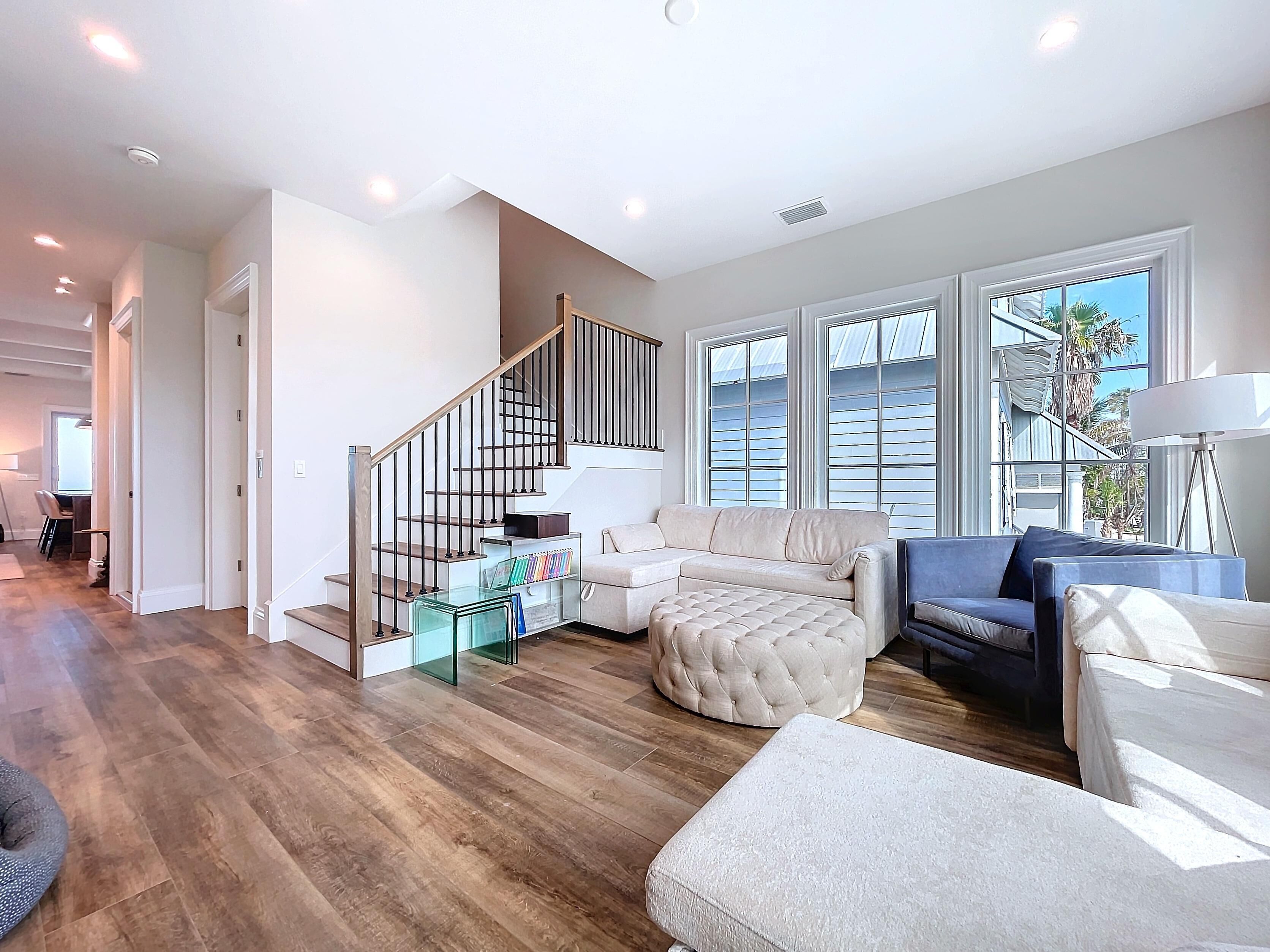 A spacious living room with a wooden floor, a beige sectional sofa, a blue sofa, and a glass coffee table.