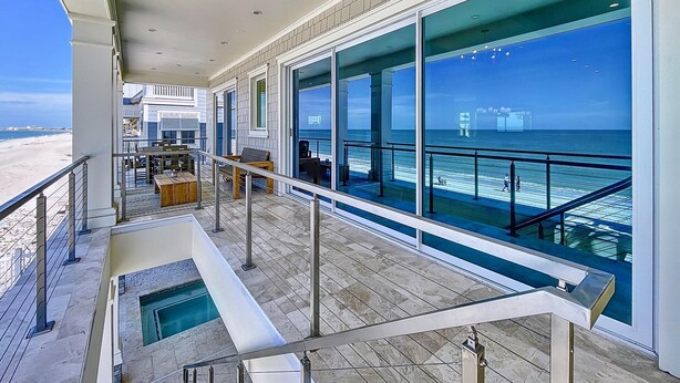 A spacious balcony with a pool, large windows offering ocean views, and a dining area with outdoor seating.