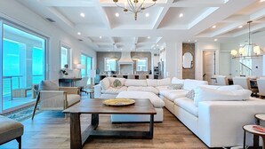 A spacious living area with a large white sectional sofa, a wooden coffee table, and a dining area with a small round table.