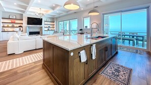 A modern kitchen with a large island, wooden cabinets, and a view of the ocean.