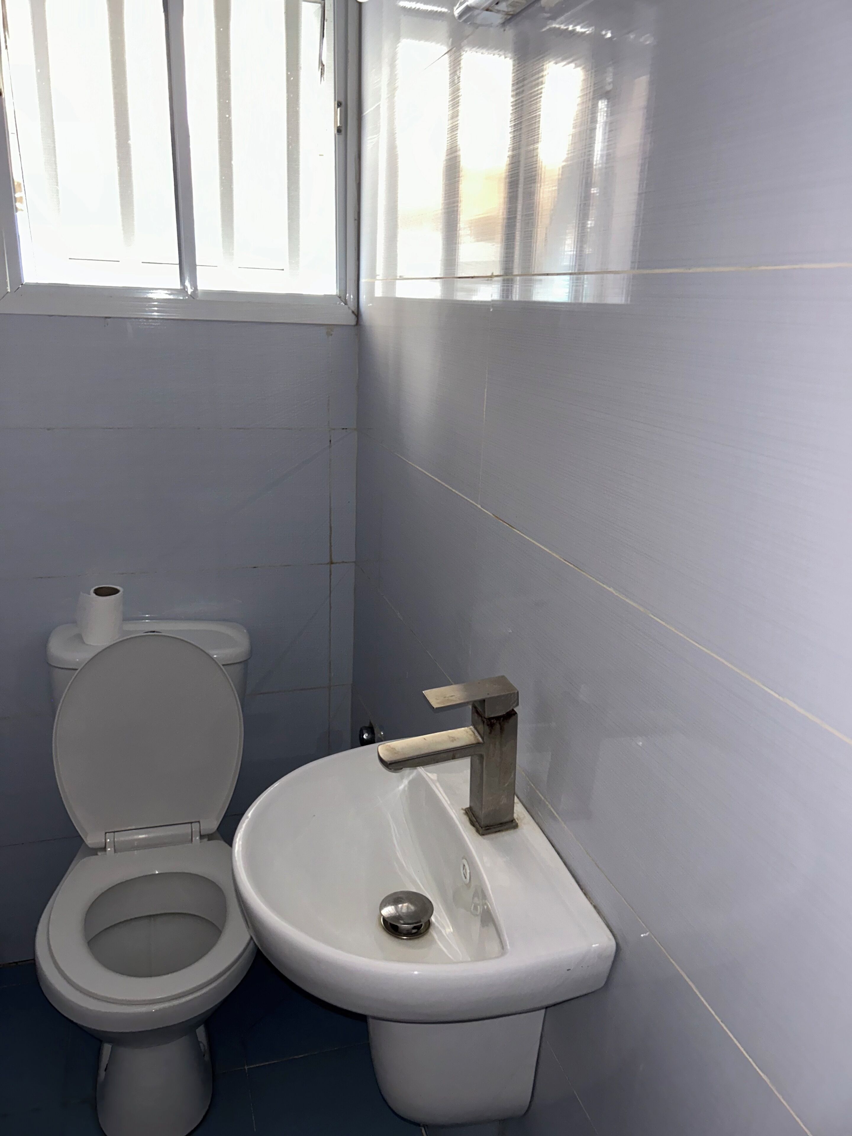 A bathroom with a toilet and sink, tiled walls, and a window.