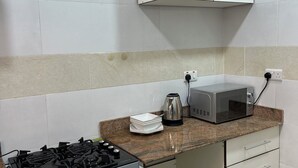 A compact kitchen with a gas stove, microwave, kettle, and a small cabinet. - Beach Side Shortlet Apartment Lekki (Lekki)