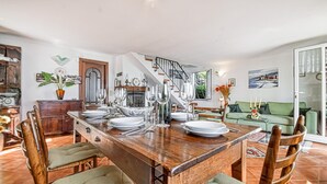 Un coin repas avec une table en bois dressée pour quatre personnes, entourée de chaises. On aperçoit un escalier au fond, qui mène à un niveau supérieur.