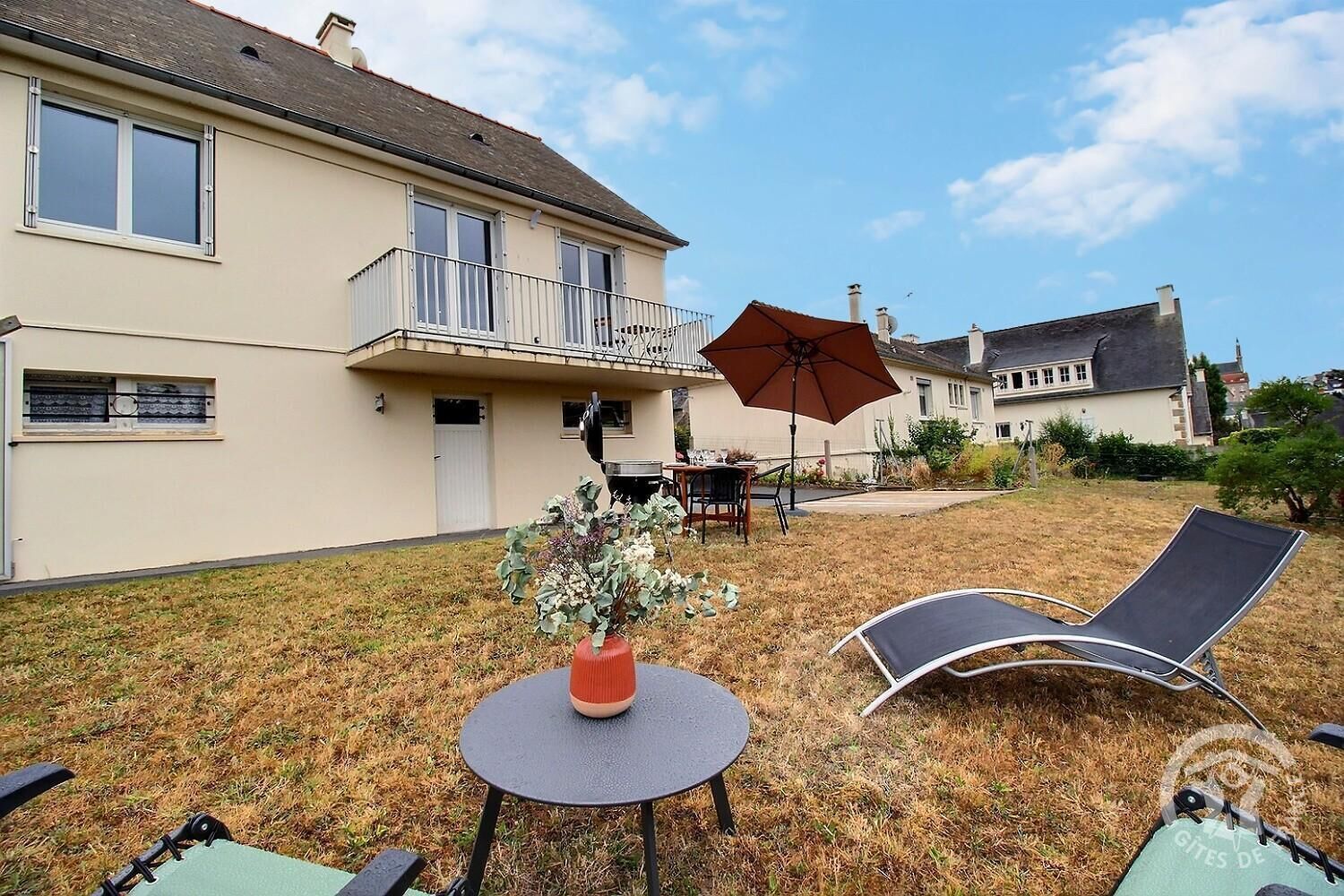 A residential property with a two-story house, a balcony, a dining area with outdoor furniture, and a lawn.