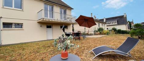 A residential property with a two-story house, a balcony, a dining area with outdoor furniture, and a lawn.
