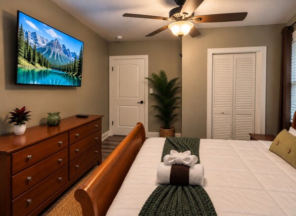 A bedroom with a bed, a dresser, a television on the wall, a ceiling fan, and a door.
