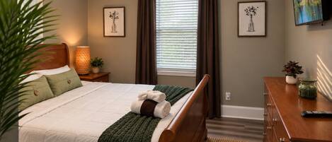 Un dormitorio con cama, mesita de noche, cómoda, televisor y ventana con cortinas.