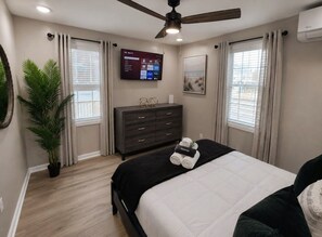 A bedroom with a bed, a dresser, a television mounted on the wall, and a ceiling fan.
