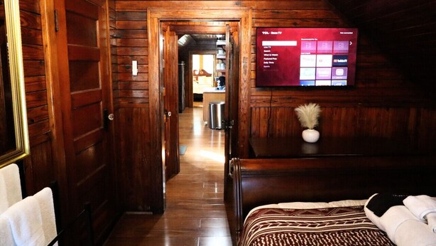 Een houten lambrisering in een gang die leidt naar een slaapkamer met een aan de muur bevestigde televisie.