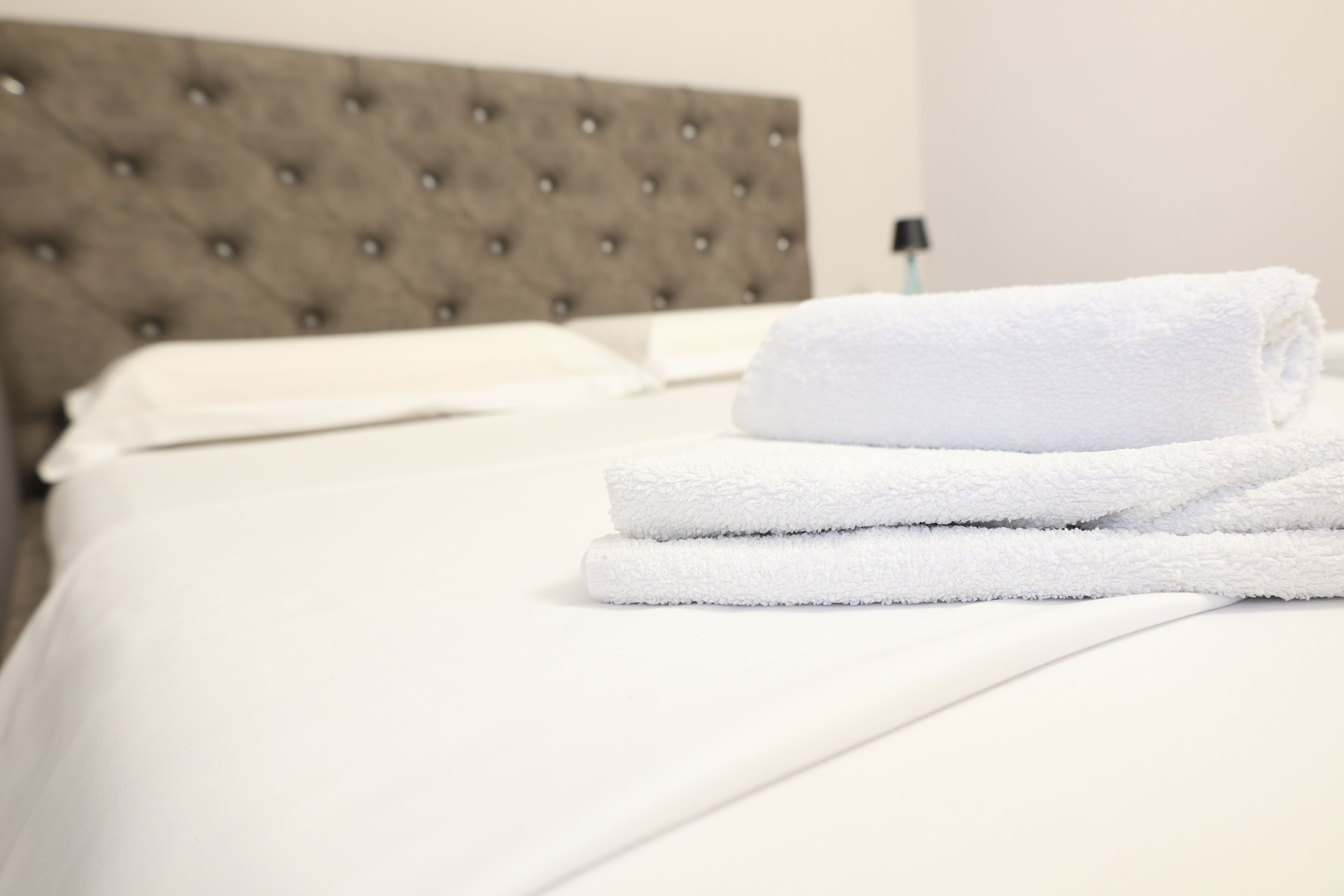 A neatly made bed with white linens and a folded white towel on top.