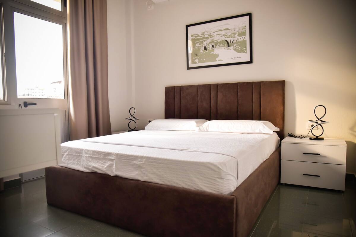 A neatly made bed with a brown headboard, a bedside table with a lamp, and a framed picture on the wall.