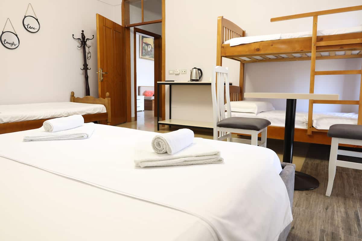 A room with two single beds, a bunk bed, a desk with a kettle, and a coat rack.