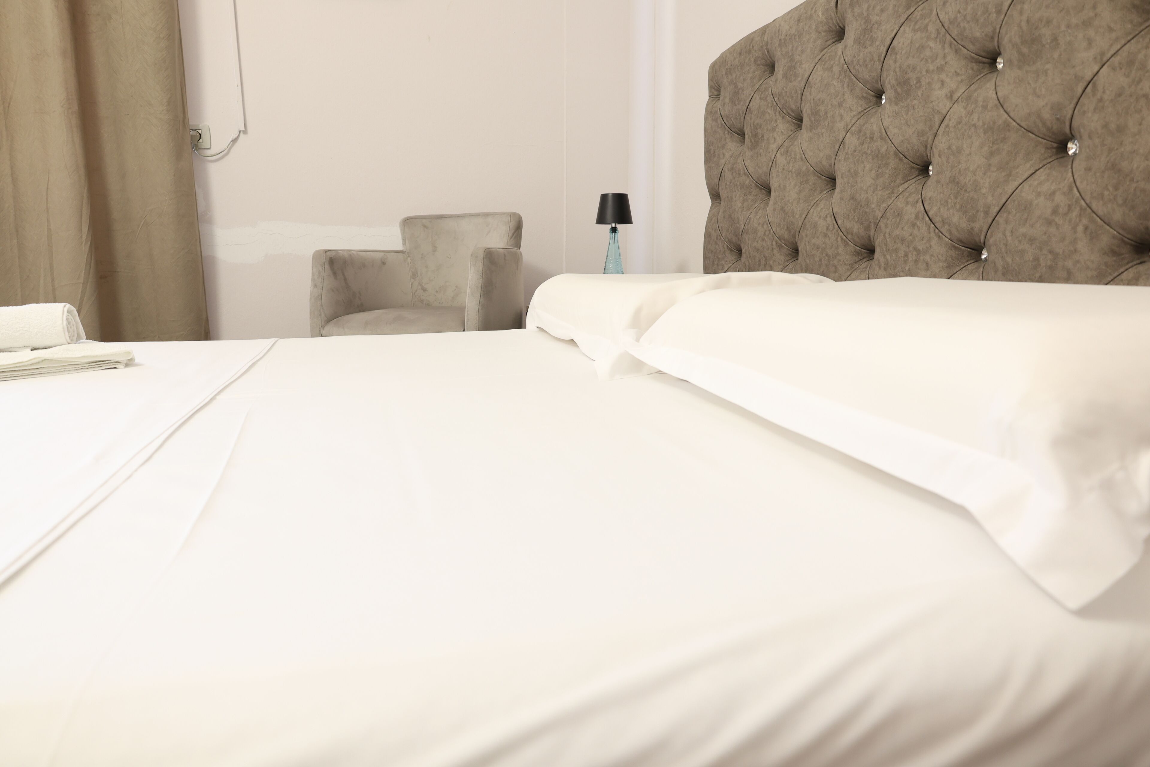 A neatly made bed with white linens and a tufted headboard.