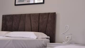 Un lit bien fait, avec du linge de lit blanc, une tête de lit marron recouverte de tissu et un tableau encadré accroché au mur.