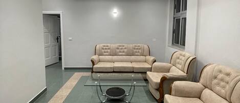 A spacious living room with a sectional sofa, a glass coffee table, and a modern ceiling light fixture.