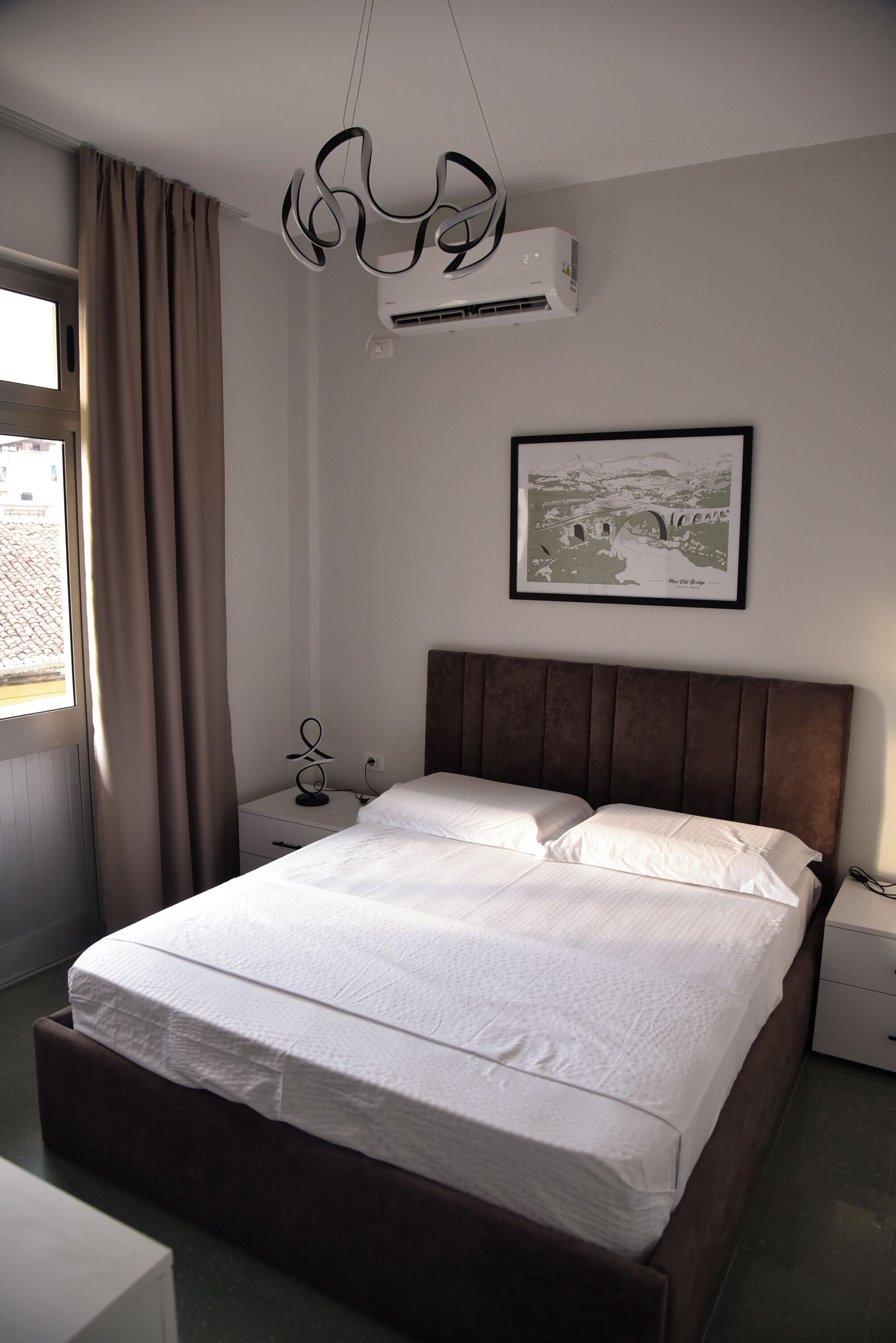 Una cama bien hecha con cabecera, una mesita de noche con lámpara y un cuadro enmarcado en la pared.