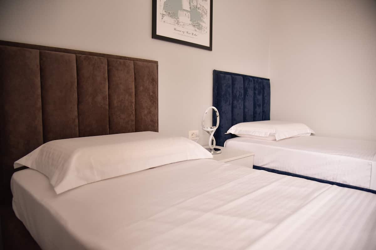 A hotel room with two beds, a brown headboard, a blue headboard, and a framed picture on the wall.