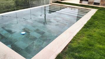 Une piscine rectangulaire à l’eau claire, entourée d’une terrasse carrelée et d’une pelouse.