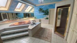 Un baño lujoso con una bañera grande, tragaluces, un mural de una playa tropical y una puerta dorada.