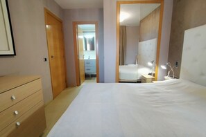 Een slaapkamer met een groot bed, een houten dressoir, een spiegel en een nachtkastje met lampen.