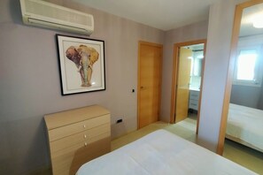 Une chambre à coucher avec un lit, une commode, un tableau encadré au mur et un appareil de climatisation.