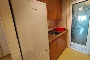 Une cuisine compacte avec un réfrigérateur Hisense blanc, des armoires en bois, un plan de travail en granit et un égouttoir à vaisselle rouge.