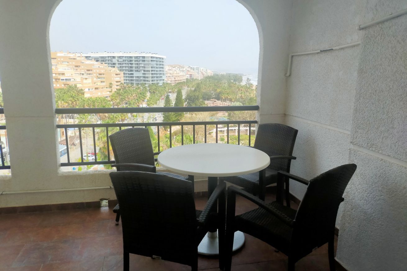 Un balcón con una mesa redonda y cuatro sillas, con vistas a un paisaje urbano con edificios y palmeras.