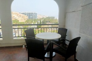 Un balcon avec une table ronde et quatre chaises, donnant sur un paysage urbain avec des immeubles et des palmiers.