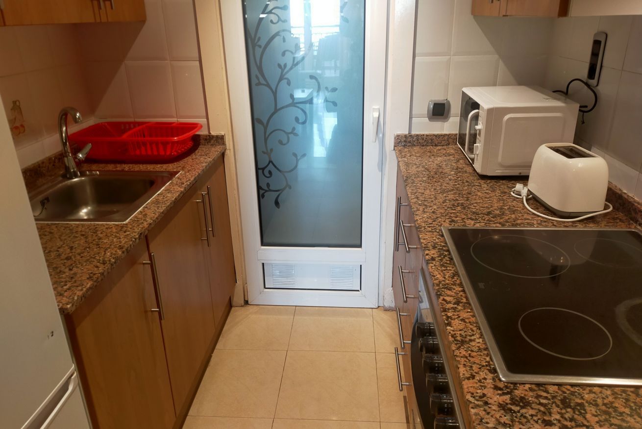 Una cocina con encimeras de granito, un lavamanos de acero inoxidable, un microondas, un tostador y una estufa.