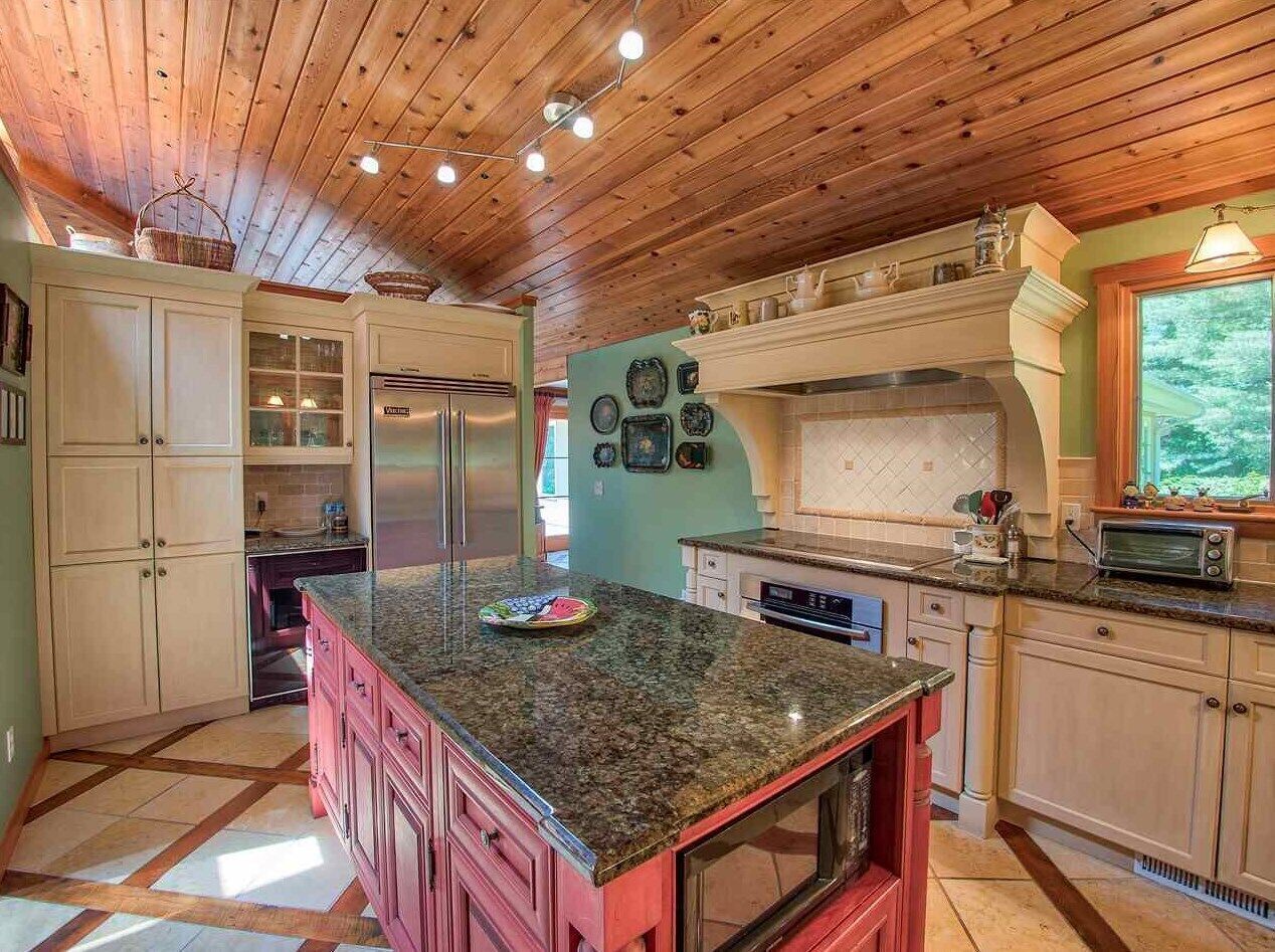 A kitchen with wooden ceiling beams, granite countertops, and a central island.