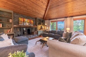 A cozy living room with a fireplace, comfortable seating, and a view of the outdoors. - Alpine Chateau Stowe-7 BR-6 bath-Game Room, Firepit, Pool! (Stowe)