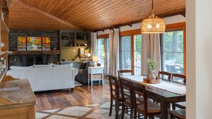 A cozy cabin interior with a wooden ceiling, a fireplace, a dining area with a table and chairs, and a view of the outdoors through large windows. - Alpine Chateau Stowe-7 BR-6 bath-Game Room, Firepit, Pool! (Stowe)