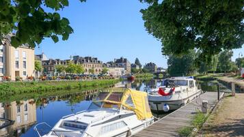 A canal with boats docked, a wooden walkway, and buildings in the background.
