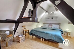 Cozy attic bedroom with a large bed, bedside tables, and a wicker chair.