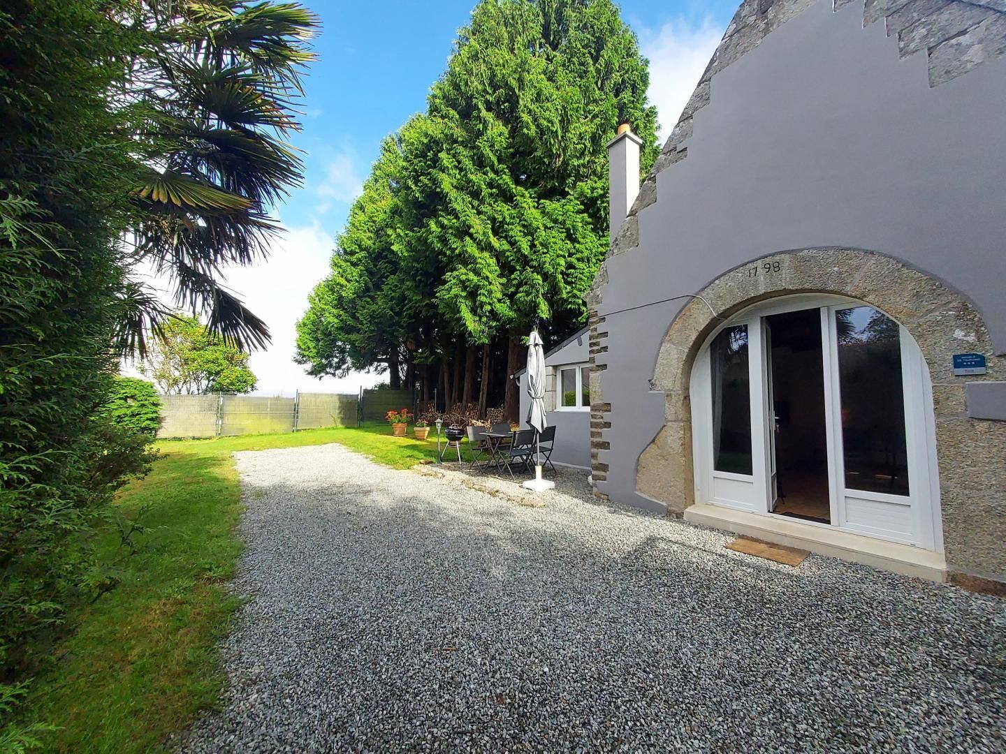 A building with a gravel driveway, a covered outdoor seating area, and a large tree in the background.